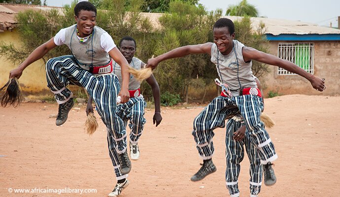 Three boys dance at a festival in Ghana.