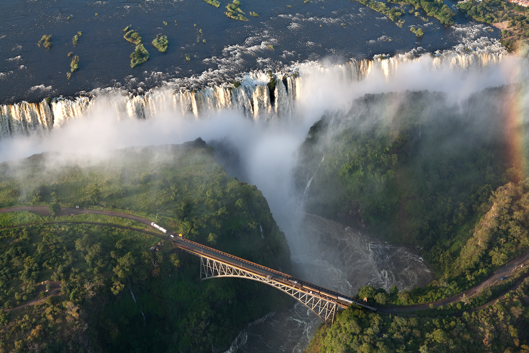 Victoria Falls in Zambia seen from above, with a bridge spannijng the river and a rainbow over the waterfall on the right