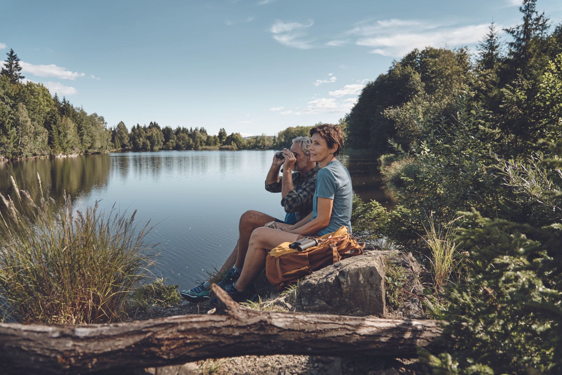 A couple sitting by a river or lake using binoculars.