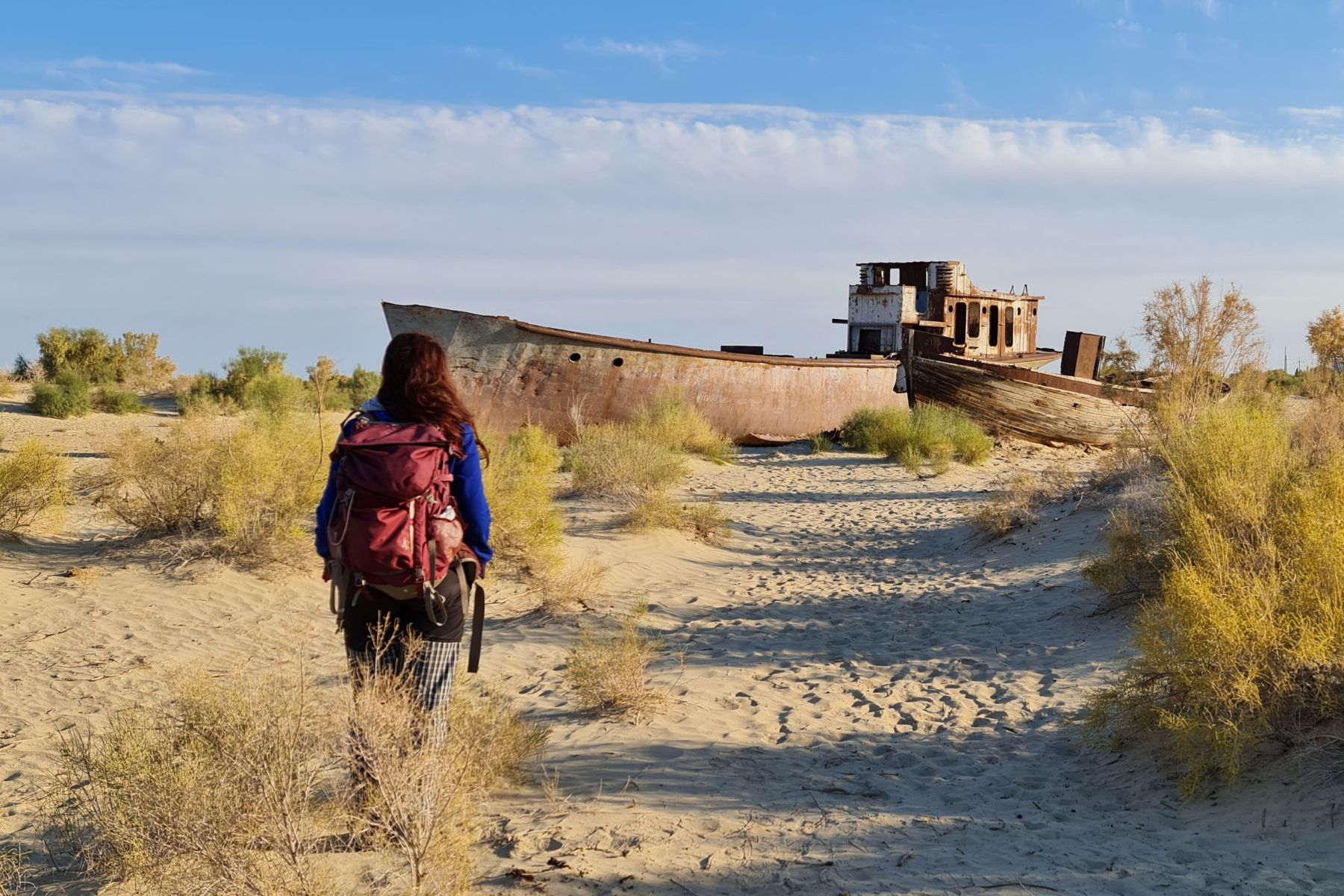 A woman approaching a shipwreck in the desert, Karakalpakstan