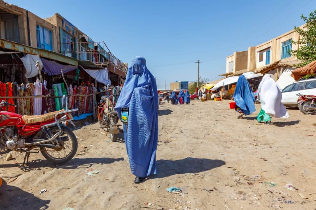 Woman walking through a market in a burka in Faryan, Afghanistan - what is it like to travel to Afghanistan?