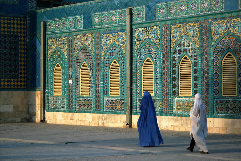 Two women in burkas walk outside of the Blue Mosque in Mazar i Sharif in Afghanistan - what is it like to travel to Afghanistan?